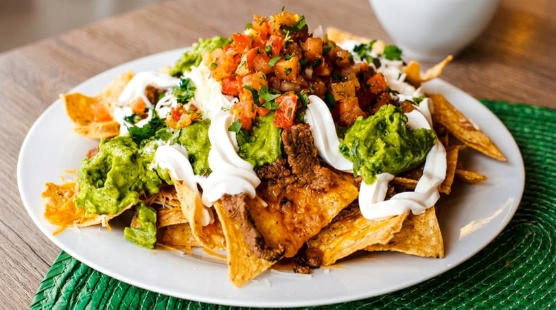 A plate of loaded nachos with steak, guacamole, sour cream, and pico de gallo.